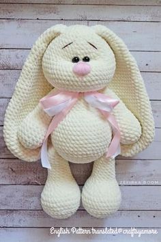 a white stuffed animal with a pink ribbon around its neck sitting on a wooden surface