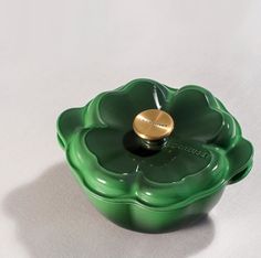 a green flower shaped bowl with a gold lid on a white tableclothed surface