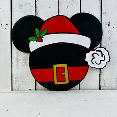 a mickey mouse christmas ornament hanging on a white wooden wall with a red and black santa hat