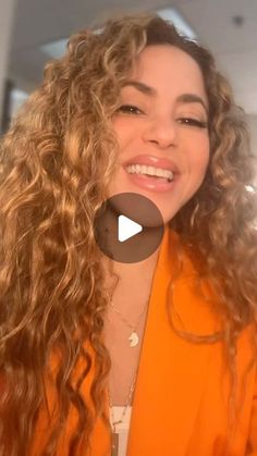 a woman with long curly hair smiling and looking at the camera while wearing an orange jacket