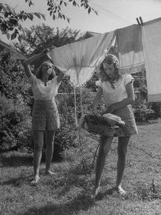 two young women hanging laundry on clothesline in the yard, 1950's or 1960s's