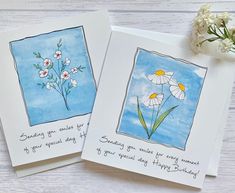 two greeting cards with flowers on them sitting next to a flower pot and white carnations