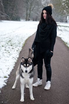 a woman standing next to a husky dog on a path in the snow with trees behind her