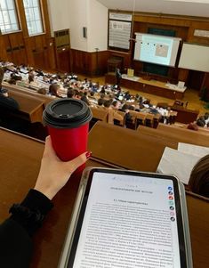 a person holding a coffee cup in front of a classroom full of students and an electronic tablet