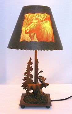 a lamp that is on top of a wooden base with a moose and pine trees underneath it