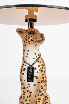 a leopard figurine sitting under a lamp on top of a wooden table with a black and white tag hanging from it's neck