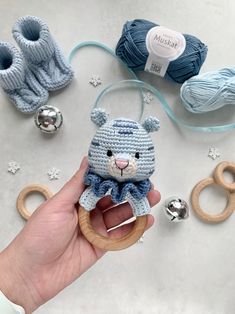 a hand holding a small crocheted teddy bear in front of yarn balls and scissors