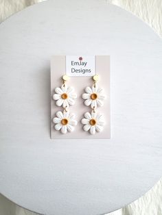 the daisy earrings are white and yellow with gold accents on them, sitting on a table