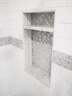 a bathroom with white and gray tile on the walls, shelves in the shower area