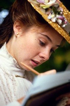 a woman reading a book while wearing a hat with flowers on it's head