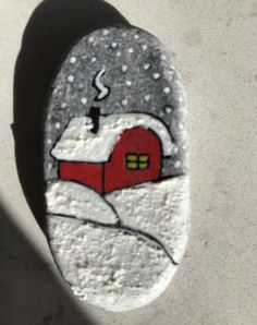 a painted rock with a red house on it's side and snow falling off the ground