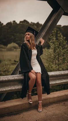 a woman in a graduation cap and gown poses on a bridge