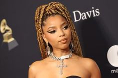 a woman with braids on the red carpet wearing a black dress and cross necklace