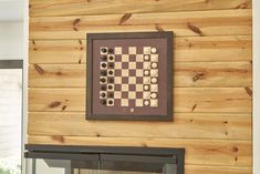 a framed chess board mounted on the side of a wooden wall next to a fire place