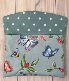 a blue purse with butterflies on it hanging from a wooden wall and white polka dots