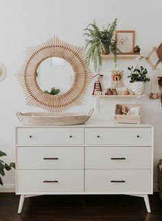 a white dresser topped with lots of plants next to a wall mounted mirror and potted plants