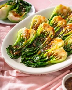 a white plate topped with green vegetables covered in sauce and seasoning next to bowls of dipping sauce