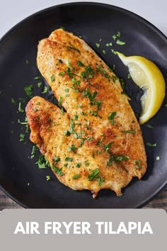 air fryer tilapia on a black plate with lemon wedges and parsley