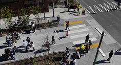 many people are walking on the sidewalk in an urban area with trees, bushes and street lights