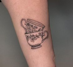 a tea cup tattoo on the left leg with flowers and leaves in it, sitting on top of a woman's arm