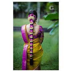 a woman wearing a yellow and purple saree with flowers in her hair is standing on the grass