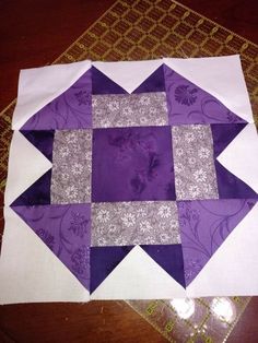 a purple and white patchwork quilt on top of a wooden table