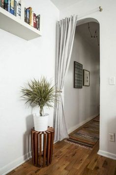 a plant in a white vase sitting on top of a wooden table next to a doorway