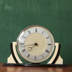 a clock sitting on top of a wooden table next to a chalkboard wall with green paint