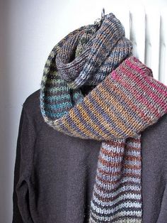 a multicolored knitted scarf hanging on a white radiator next to a black shirt