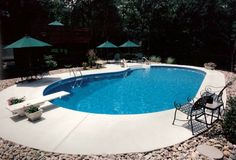 an empty swimming pool with chairs and umbrellas in the back yard, surrounded by rocks