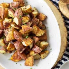 a white plate topped with cooked potatoes on top of a wooden table next to bread