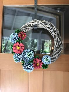 a wreath made out of paper flowers on a front door with a window in the background