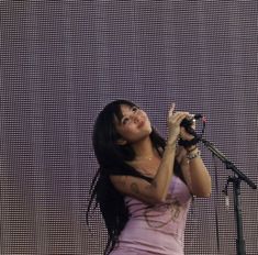 a woman standing in front of a microphone on top of a stage wearing a pink dress