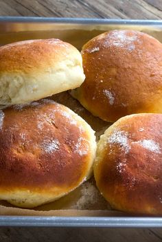 four rolls sitting on top of a pan covered in powdered sugar