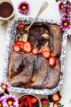 a cake with strawberries and powdered sugar on it next to some pink flowers