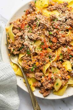 a white plate topped with pasta covered in meat sauce and parmesan cheese next to a fork