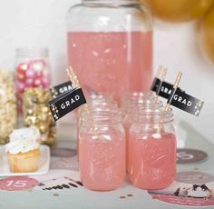 there are some pink drinks in mason jars with black labels on them and cupcakes to the side