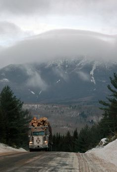 a truck driving down a snow covered road with mountains in the backgrouund