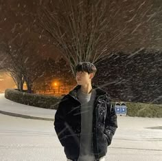 a young man standing in the middle of a snow storm with his skateboard under his arm