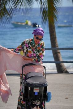 a woman is pushing a stroller with a pink scarf on it's back