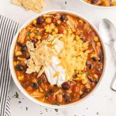 two bowls filled with chili, beans and tortilla chips on top of a white table