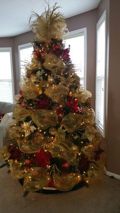 a christmas tree decorated with gold and red ornaments in a living room area next to a window