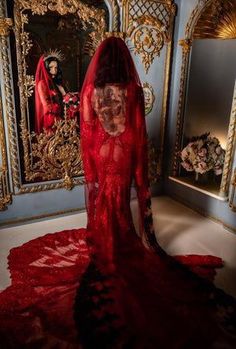 a woman in a red wedding dress standing next to a wall with ornate paintings on it