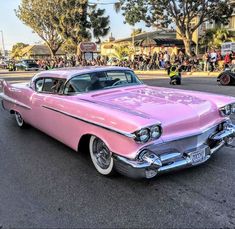 an old pink car is parked on the side of the road with people in the background