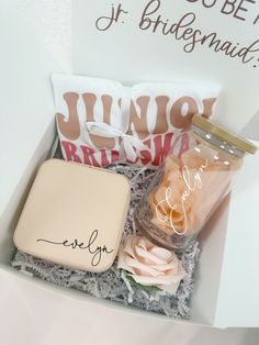 an open box with some pink flowers and a small jar in the middle, on top of a white table