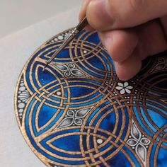 a hand is drawing on a piece of paper with gold and blue designs in it