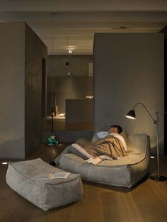 a man laying on top of a bed in a living room next to a lamp