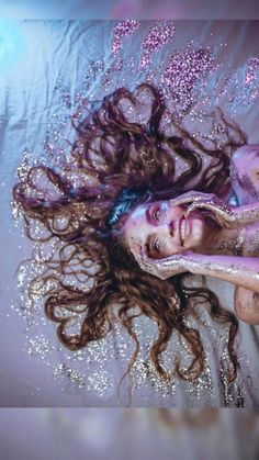 a woman with long hair laying on top of a bed covered in water and glitter