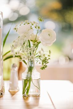 white flowers in a clear vase on a table next to an empty glass bottle and salt shaker