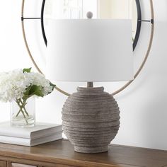 a table with a lamp and flowers on it in front of a mirror that has a circular frame around it